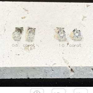 Puede incluir: Dos pares de pendientes de bot&oacute;n con corte ovalado en tono plateado. Un par est&aacute; etiquetado como 0,5 quilates y el otro como 1,0 quilates. El texto incluye amelia minimalist, CLASSIC Oval, Oval Cut, 0,5 Ct each weight 4x6mm y 1,0 Ct each weight 5x7mm.