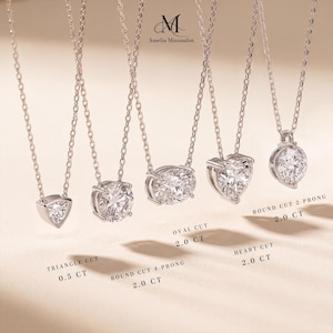 May include: Five silver-toned necklaces with clear faceted stones in triangle, round, oval, heart, and round cuts. Text labels indicate: Triangle Cut 0.5 CT, Round Cut 4-Prong 2.0 CT, Oval Cut 2.0 CT, Heart Cut 2.0 CT, and Round Cut 2-Prong 2.0 CT.