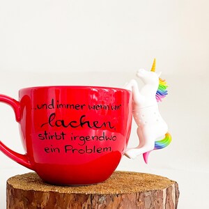 Könnte beinhalten: Rote Keramiktasse mit einem weißen Einhorn-Tee-Infuser. Die Tasse hat den Text "...und immer wenn wir lachen, stirbt irgendwo ein Problem." aufgedruckt.