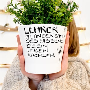Könnte beinhalten: Ein weißer Keramik-Pflanztopf mit schwarzem Text, der "Lehrer pflanzen samen des wissens die ein leben wachsen." lautet. Der Topf enthält eine kleine grüne Pflanze mit weißen Blüten.