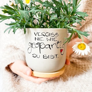 Könnte beinhalten: Eine graue Keramiktasse mit einem Untersetzer aus Holz. Die Tasse hat einen schwarzen Schriftzug mit der Aufschrift "Vergiss nie wie großartig du bist." mit einem kleinen roten Herzen.