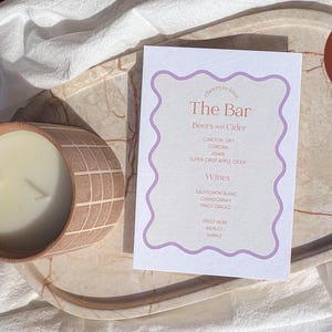 May include: A printable bar menu with a purple border and a list of beers, ciders, and wines. The text "cheers to life" is at the top of the menu and the text "The Bar" is in a larger font size.
