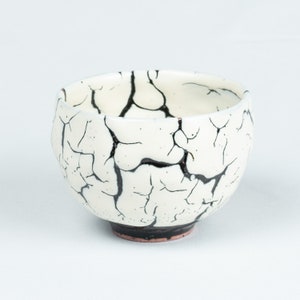 May include: White ceramic bowl with a black crackle glaze. The bowl has a rounded shape and a small foot.