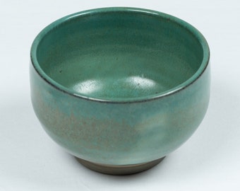 May include: A small, green ceramic bowl with a speckled glaze. The bowl is round and has a slightly flared rim.