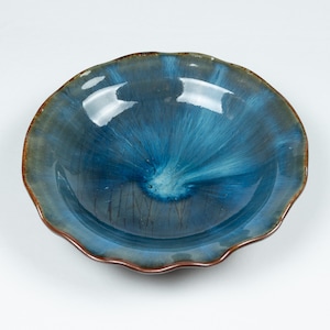 Puede incluir: Un cuenco de cerámica azul con un borde ondulado y un esmalte azul y blanco. El cuenco tiene un diseño único con un patrón de remolino en el centro.