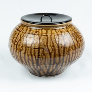 May include: A brown ceramic jar with a black lid and a textured surface. The jar has a wide mouth and a rounded body.