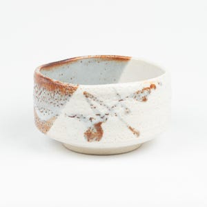 May include: A handcrafted ceramic bowl with a textured white exterior and a brown rim. The bowl features a unique design with brown and blue accents, perfect for serving soups or other dishes. The bowl is approximately 4 inches in diameter.