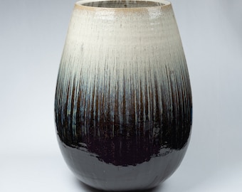 May include: A large, white and black ceramic vase with a rounded, bulbous shape. The vase has a white glaze on the top half and a black glaze on the bottom half, with a gradient of blue and white in between.
