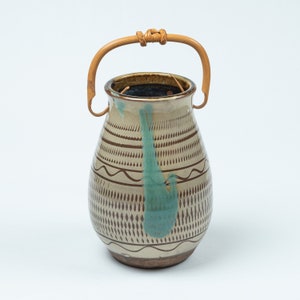 May include: A brown and white ceramic vase with a blue and green glaze design. The vase has a woven bamboo handle.