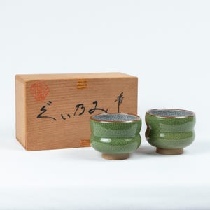 May include: Two green ceramic teacups with a crackled glaze and a silver rim, in a wooden box with Japanese writing that says "ぎんざ"