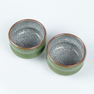 May include: Two green ceramic teacups with a crackle glaze and a copper rim.