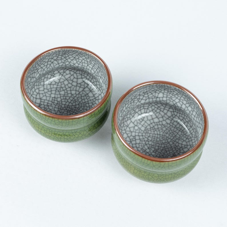 May include: Two green ceramic teacups with a crackle glaze and a copper rim.