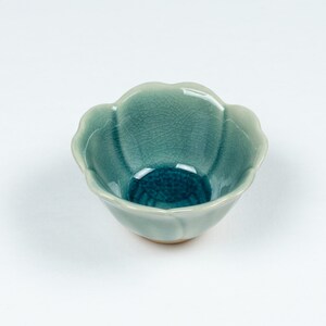 May include: A small, teal blue ceramic bowl with a flower-shaped rim. The bowl has a crackled glaze and a smooth, glossy finish.