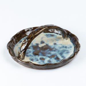 May include: A brown ceramic serving tray with a white and blue glaze. The tray has a scalloped edge and a woven handle.