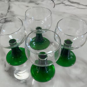May include: A set of four clear glass goblets, each featuring a rounded bowl and a distinct stem with a ribbed, dark green texture that transitions into a smooth, vibrant green circular base, providing a stable foundation for each glass.