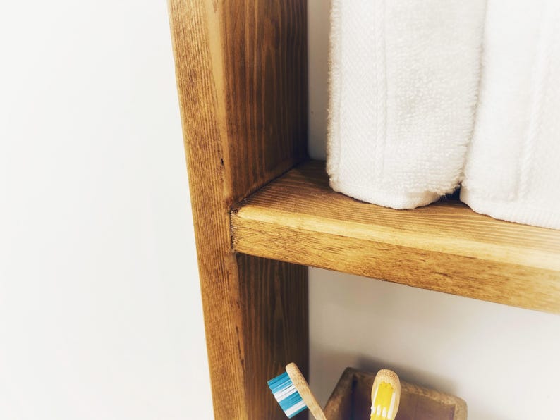 May include: A wooden shelf unit with two shelves. The top shelf has two white towels folded on it. The bottom shelf has two toothbrushes.