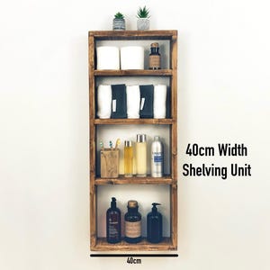 May include: A 40-inch wide wooden shelf unit with four shelves. The shelves are filled with various items, including towels, bottles, and a small plant. The shelf unit is mounted on a white wall.