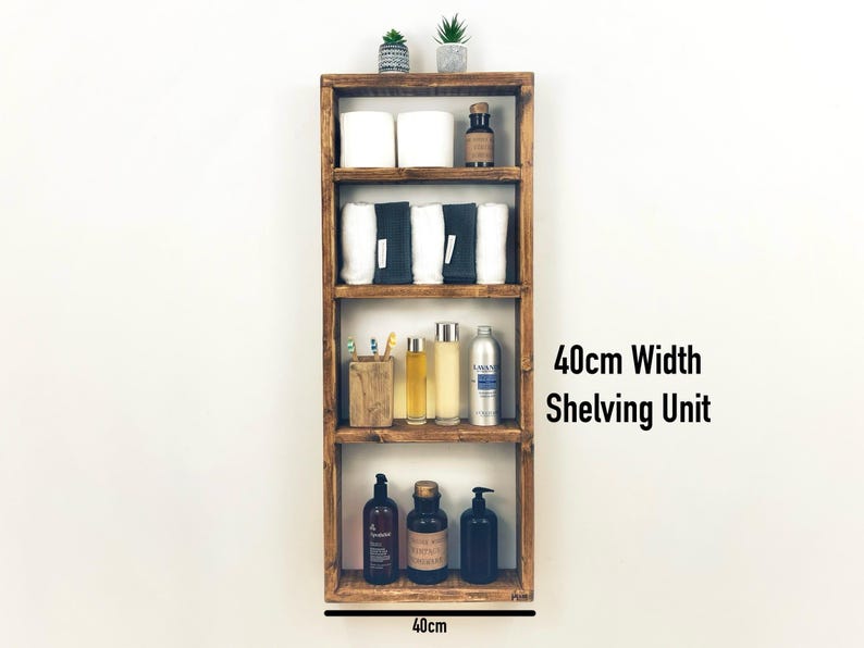 May include: A 40-inch wide wooden shelf unit with four shelves. The shelves are filled with various items, including towels, bottles, and a small plant. The shelf unit is mounted on a white wall.