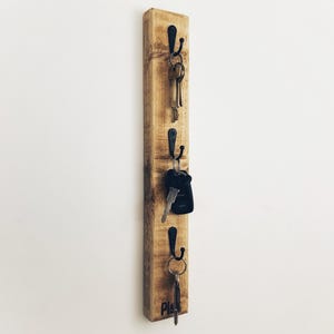 May include: A wooden key holder with four hooks and the word "Play" engraved on the bottom. Keys are hanging on the hooks.