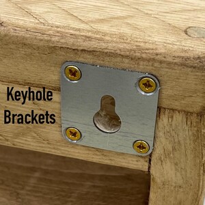 May include: Close-up of a wooden shelf with a metal keyhole bracket attached. The bracket has four screws and a keyhole opening. The text "Keyhole Brackets" is printed on the wood.