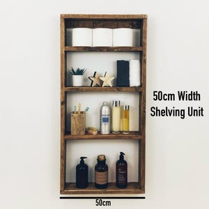 May include: A rustic wooden shelf unit with four shelves, measuring 50cm wide. The shelves are filled with various items, including toilet paper, plants, toiletries, and decorative stars. The unit is labeled "50cm Width Shelving Unit".