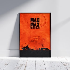 May include: Framed poster featuring the text "MAD MAX FURY ROAD" in black against a fiery orange background. Silhouetted vehicles and explosions are visible at the bottom, creating a dramatic scene.