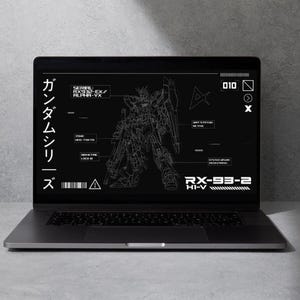 May include: A silver laptop displays a schematic of a Gundam robot on its screen. The screen features white text and line drawings against a black background. Japanese characters are visible on the left side of the screen.