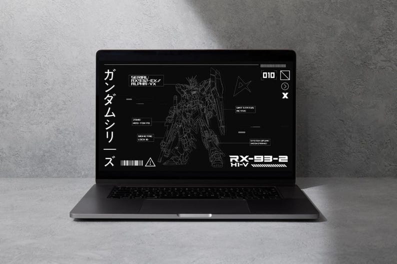 May include: A silver laptop displays a schematic of a Gundam robot on its screen. The screen features white text and line drawings against a black background. Japanese characters are visible on the left side of the screen.