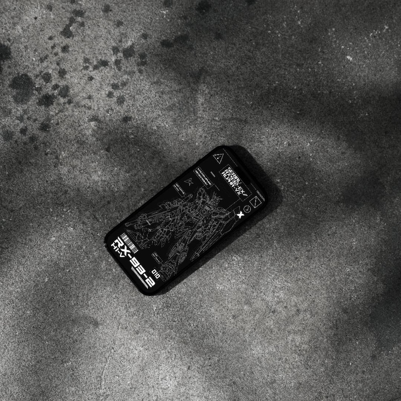 May include: Black smartphone case featuring a detailed white schematic of a robot, with the text "RX-93-2" and other technical markings. The case is lying on a textured gray surface.