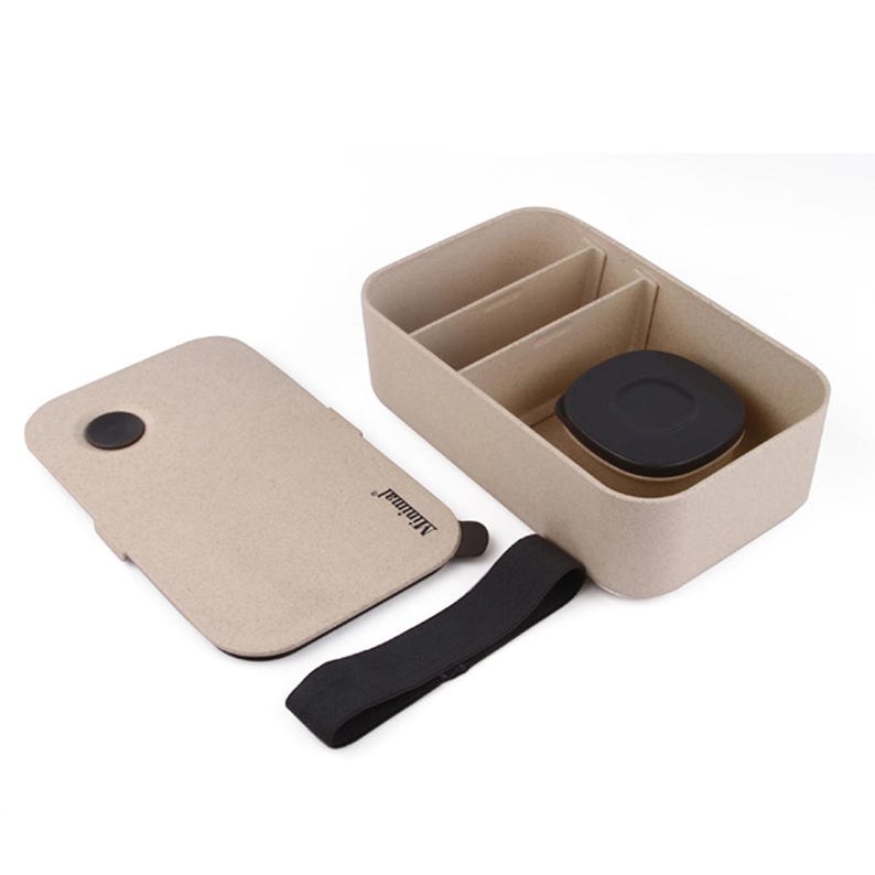 May include: A rectangular beige bento box with a speckled texture, featuring a removable lid with the text Minimal, a black elastic strap, two internal dividers, and a small circular black container with a lid nestled inside the main compartment.