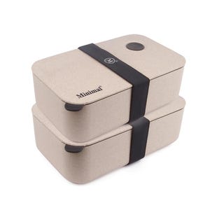 May include: A stack of two rectangular beige bento boxes with rounded corners. A black elastic band secures the containers together. The top lid features a circular brown accent and the text Minimal with a logo on the band and the side.