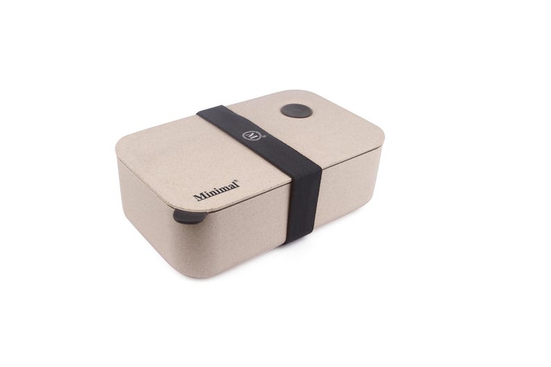 May include: A rectangular beige bento box with a speckled texture, featuring a black elastic band wrapped around the center. The word Minimal is printed in black on the lid, along with a small circular black logo on the band and a circular vent.