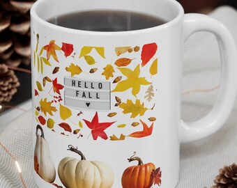 May include: White ceramic mug with a fall-themed design featuring colorful leaves, pumpkins, and the text "HELLO FALL" with a heart. The mug is filled with coffee and is sitting on a table with a white tablecloth.