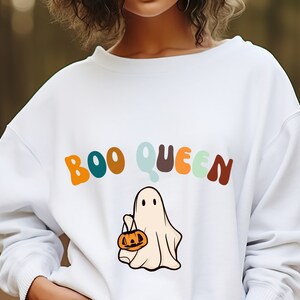Può includere: Felpa bianca con il testo "BOO QUEEN" in lettere colorate e un fantasma dei cartoni animati che tiene una zucca.