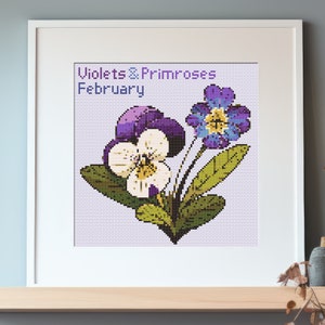 May include: A framed cross-stitch design featuring a bouquet of purple and white pansies and blue primroses. The text "Violets & Primroses February" is above the flowers.