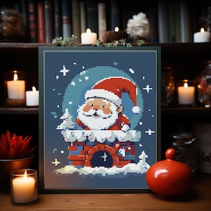 May include: A framed cross-stitch design featuring Santa Claus in a red suit and hat, climbing down a chimney. The background is a blue night sky with white snowflakes and stars. The design is surrounded by a green frame.