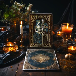 A digital render of 'The Lovers' Tarot cross stitch design. Presented in the format of tarot card on a table with candles. Strong black, white and blue DMC thread colours.