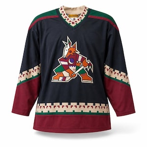May include: Navy blue hockey jersey with a colorful coyote logo on the front. The jersey has maroon sleeves and green and maroon accents on the shoulders and hem. The neckline features a decorative pattern and the word "KOHO".