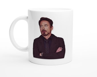 Könnte beinhalten: Weiße Keramiktasse mit einem aufgedruckten Bild eines Mannes mit einem ernsten Gesichtsausdruck. Der Mann trägt einen dunklen Anzug und eine Krawatte. Die Tasse hat eine Standardgröße.
