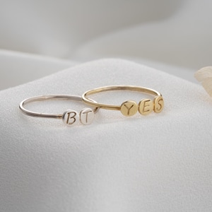 Könnte beinhalten: Zwei filigrane Ringe, einer silberfarben und einer goldfarben, werden gezeigt. Der silberne Ring buchstabiert "BT", während der goldene Ring "YES" buchstabiert. Die Ringe haben dünne Bänder mit kleinen, kreisförmigen Buchstaben.