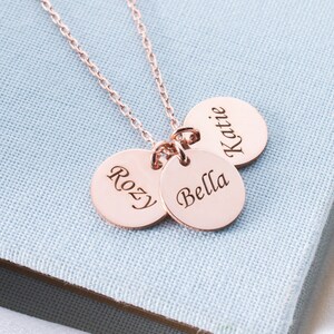 May include: A rose gold necklace with three round charms engraved with the names "Katie", "Bella", and "Rozy".