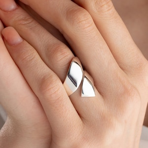 May include: A silver ring with a unique, geometric design. The ring is made of two overlapping, curved pieces that form a pointed shape.