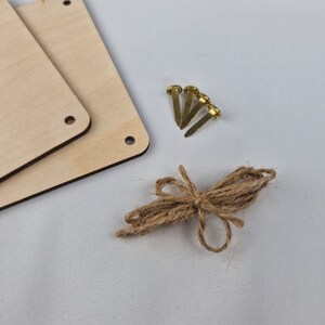 May include: Two unfinished wooden squares with holes in the corners, four gold tacks, and a length of twine tied in a bow.