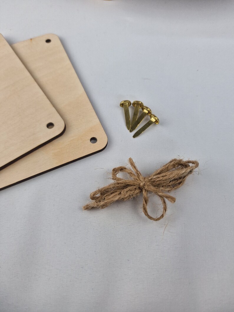 May include: Two unfinished wooden squares with holes in the corners, four gold tacks, and a length of twine tied in a bow.