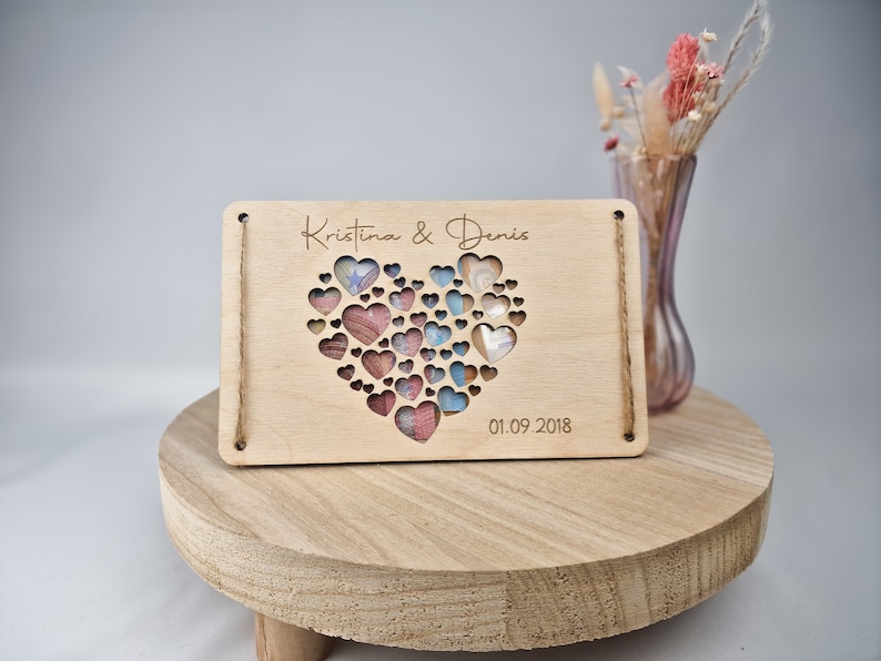 May include: A wooden plaque with a heart-shaped cutout filled with colorful hearts. The plaque is engraved with the names "Kristina & Denis" and the date "01.09.2018".