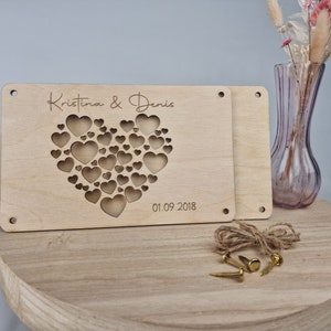 May include: Wooden heart-shaped sign with the names "Kristina & Denis" and the date "01.09.2018" engraved on it. The heart is made up of smaller hearts, creating a unique design.