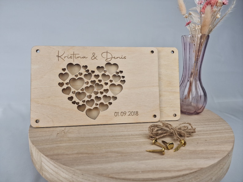May include: Wooden heart-shaped sign with the names "Kristina & Denis" and the date "01.09.2018" engraved on it. The heart is made up of smaller hearts, creating a unique design.