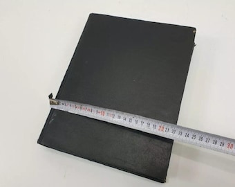 May include: A black, hardback book with a plain cover. The book is lying flat on a white surface with a tape measure beside it.