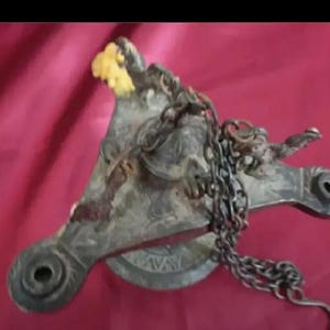 May include: An antique brass oil lamp with intricate designs and a chain hanging from it. The lamp has a round base and three arms, each with a small hole at the end. The lamp is in a worn condition, with some areas showing signs of rust.