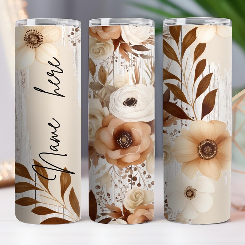 May include: A set of three white and brown floral patterned tumblers with a woodgrain background. The tumbler on the left has the text "Name here" written on it.